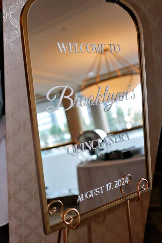 Welcome sign in elegant script for Brooklyn's Quincea&ntilde;era event on August 17, 2024, featuring decorative mirror and gold frame.