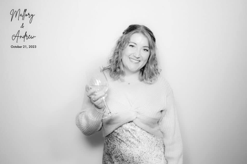 Wedding guest enjoying photo booth with wine glass, personalized backdrop and Calgary wedding details.