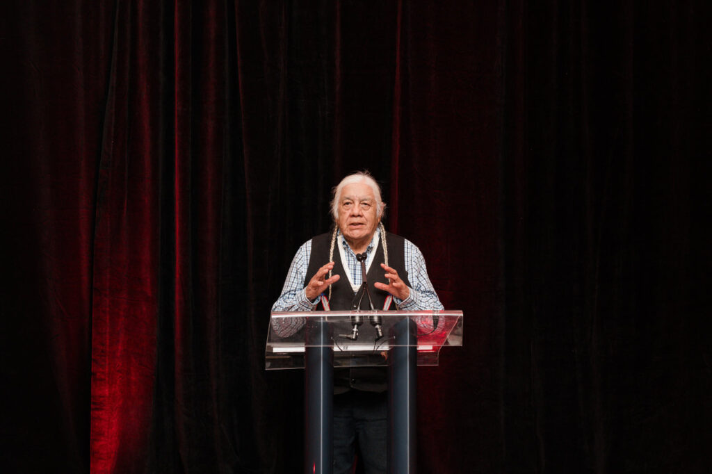 Elder speaking at podium during CCA AGM & Banquet Dinner, emphasizing reconciliation and community values.
