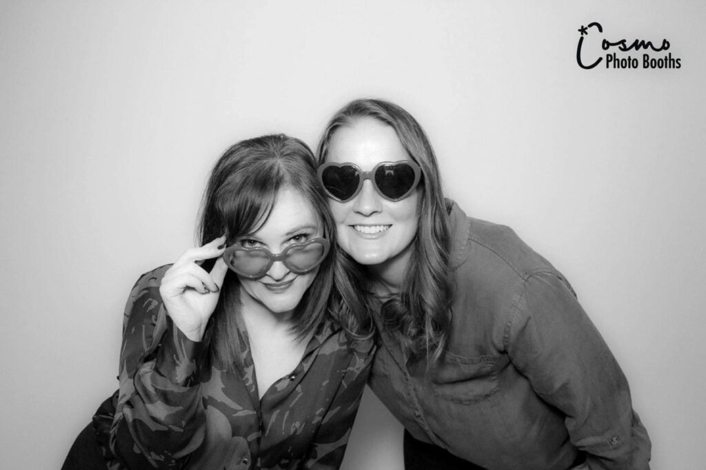 Two women posing playfully in stylish sunglasses, showcasing a fun moment captured in a Glam Booth photo experience by Cosmo Photo Booths.