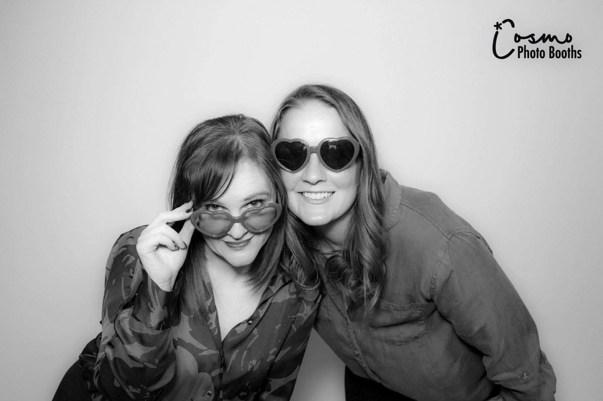 Two women posing playfully in stylish sunglasses, showcasing a fun moment captured in a Glam Booth photo experience by Cosmo Photo Booths.