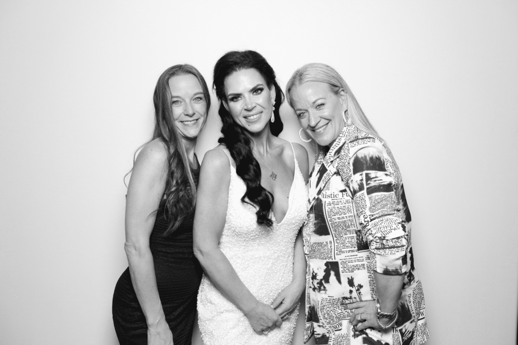 Three smiling wedding guests posing in a mirror photo booth.