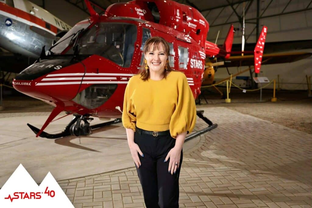 Woman in a yellow blouse posing in front of a red helicopter, showcasing event photography for celebrations and gatherings.