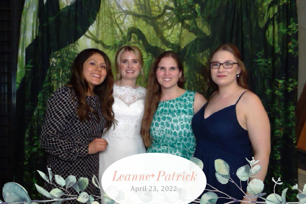 Four women posing together at a wedding photo booth, celebrating Leanne and Patrick's special day on April 23, 2022, with a lush green jungle backdrop.