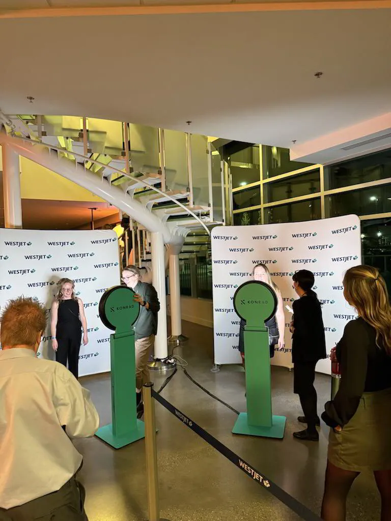 Guests interacting with photo booths at the WestJet Holiday Party activation, featuring branded backdrop and vibrant lighting.