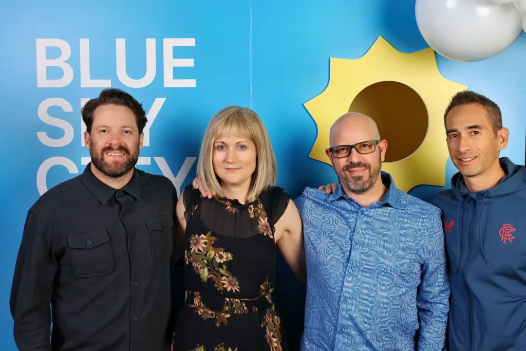 Group of four people posing together in front of a bright blue backdrop with the text "BLUE SKY CITY," showcasing a joyful atmosphere typical of event photography.