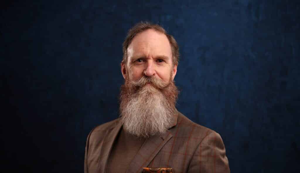 Man with a distinguished beard and a stylish blazer, posing against a dark blue backdrop, showcasing professional headshot photography for private events and celebrations.