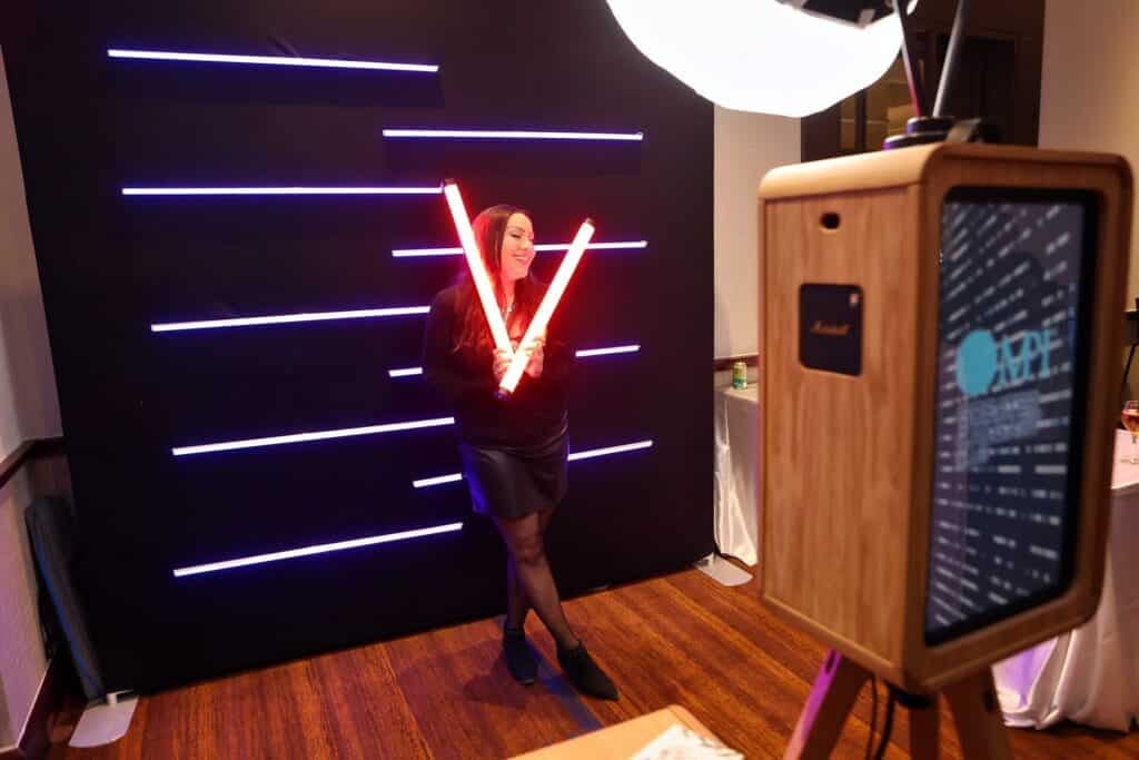 Woman posing with glowing LED lights in front of a dark backdrop, featuring the Glow Booth, showcasing vibrant lighting and an interactive photo experience for events.