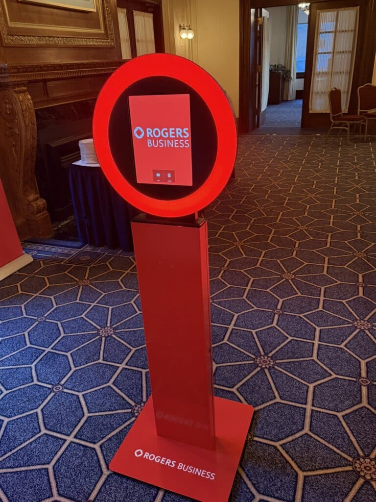 Branded photo booth with illuminated red circle and "ROGERS BUSINESS" logo, set in an elegant event space, highlighting custom photo experiences for brand visibility.