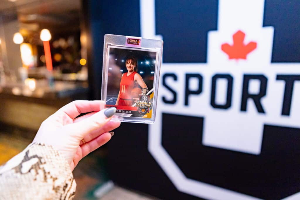 Woman's hand holding up a UofC trading card at a sports event