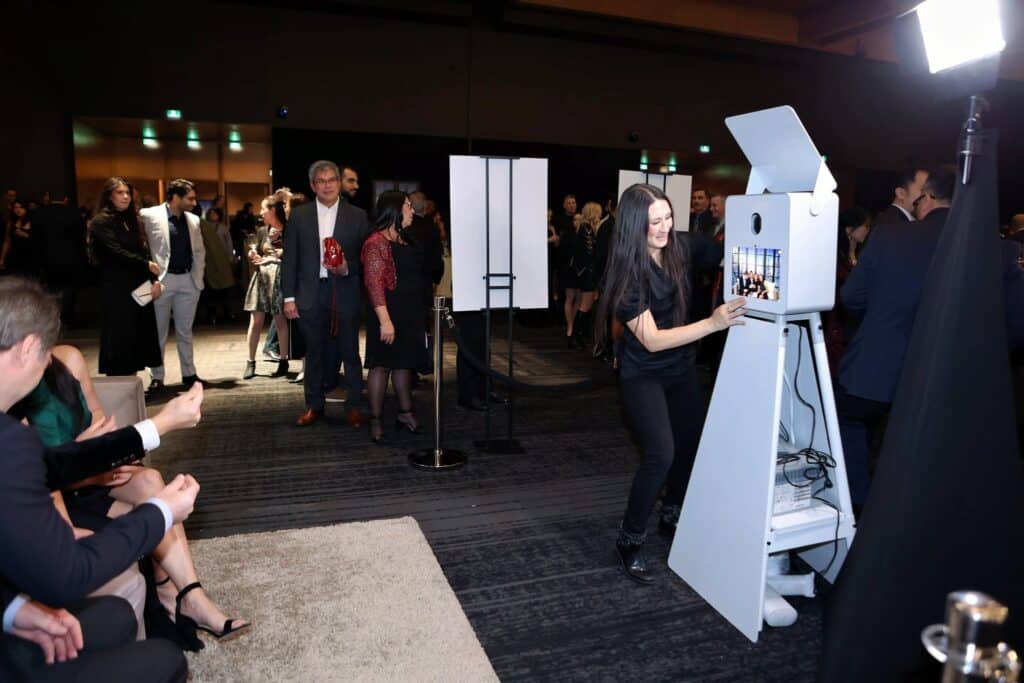 Photo booth setup at an event in Calgary with a woman operating the booth, guests mingling in the background, capturing fun moments and keepsakes.