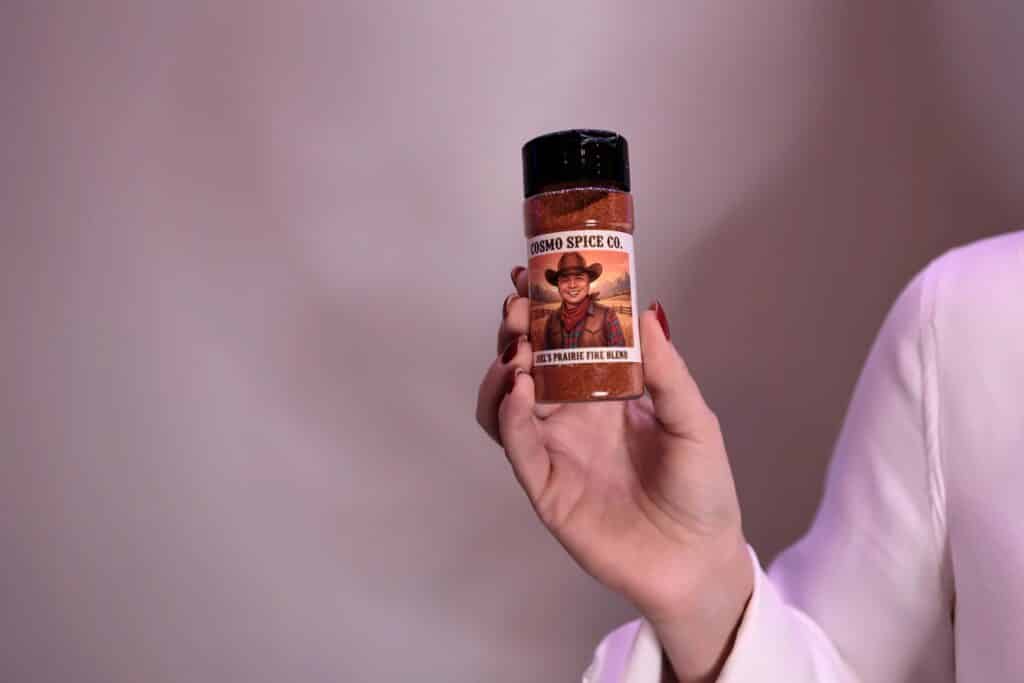 Personalized spice label from Cosmo Spice Co. held by a hand, featuring a cowboy image, highlighting custom takeaways from the FAM tour at Calgary TELUS Convention Centre.