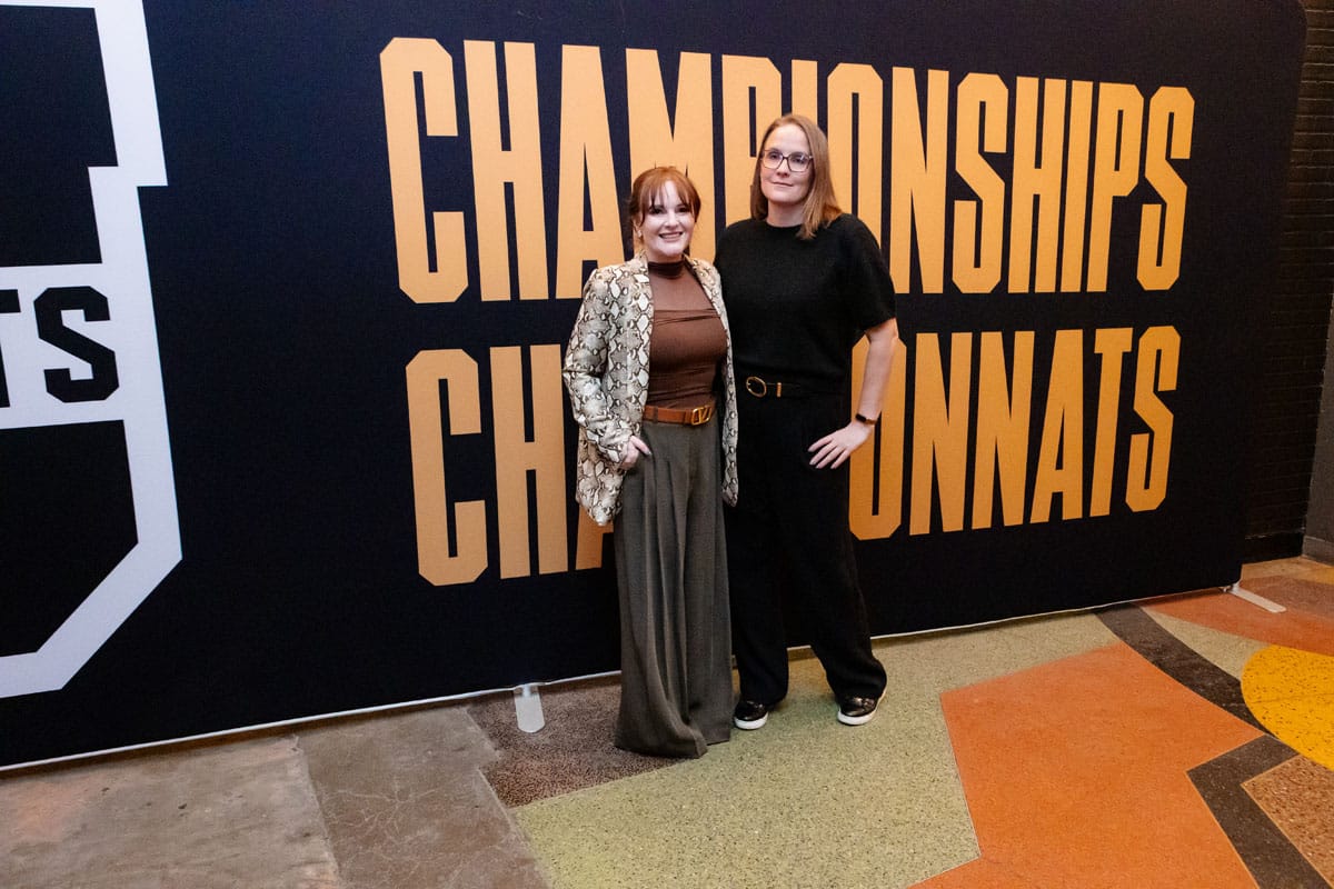 Two women posing in front of a backdrop featuring the words "CHAMPIONSHIPS" and "CHAMPIONNATS," representing a celebratory event atmosphere.