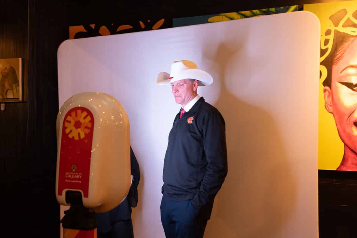 Man wearing a cowboy hat posing in front of a photo booth backdrop at an event, showcasing a unique photo experience.