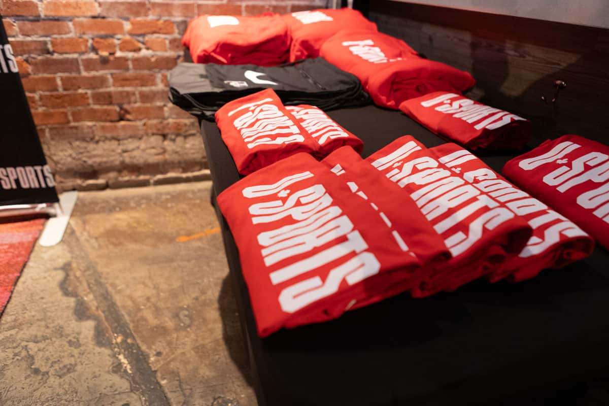 Red and black folded t-shirts displaying "U SPORTS" logo on a table, set against a brick wall backdrop, showcasing event merchandise for the U SPORTS Men’s Final 8 Gala.