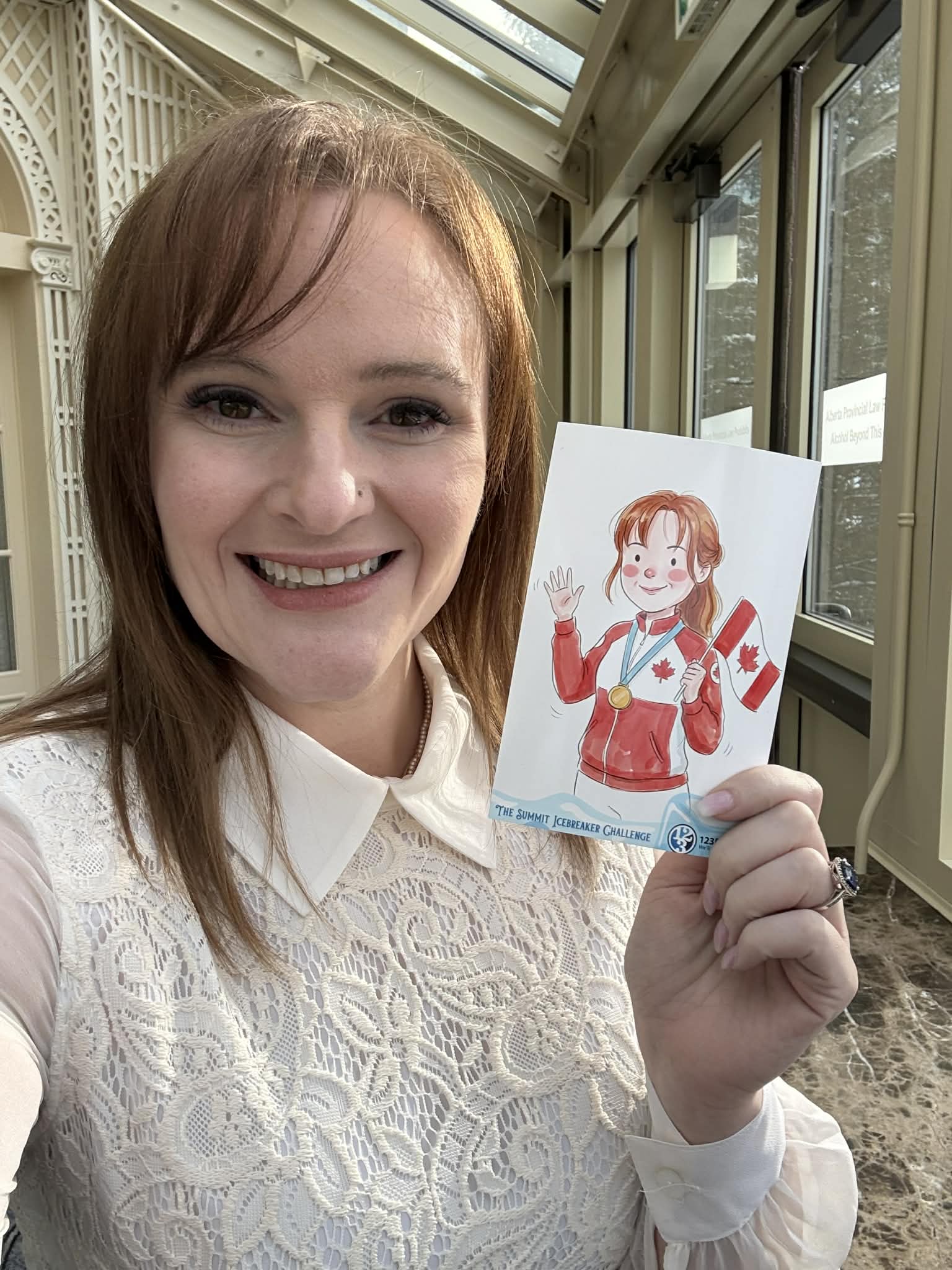 Woman smiling and holding an illustrated card featuring a character in Canadian attire with a medal, set in a bright indoor environment, reflecting engagement and participation at an event.