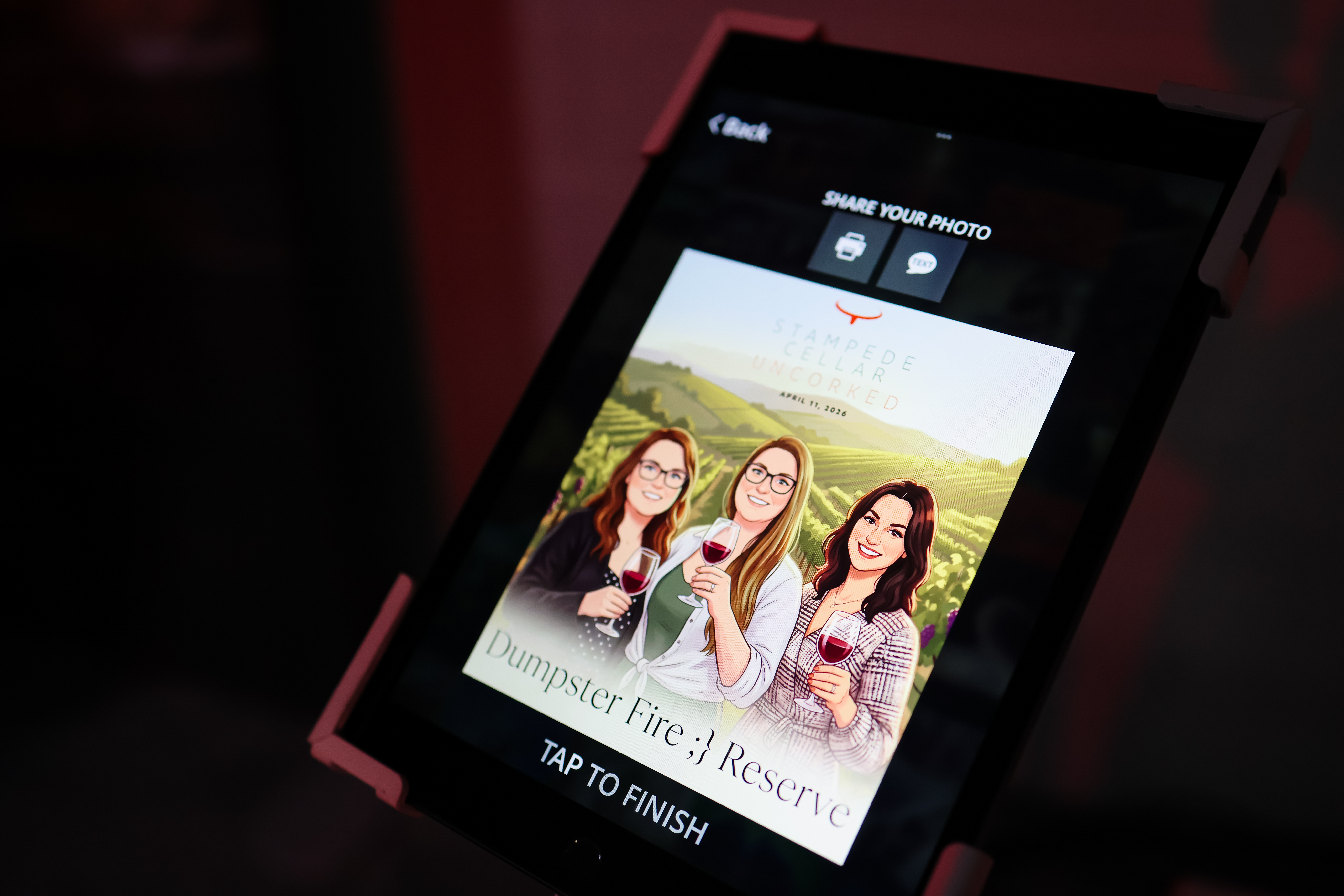 Custom wine label featuring three women holding glasses of wine, with the text "STAMPede Cellar UNCORKED" and "Dumpster Fire Reserve," set against a vineyard backdrop, illustrating the interactive photo booth experience at the event.