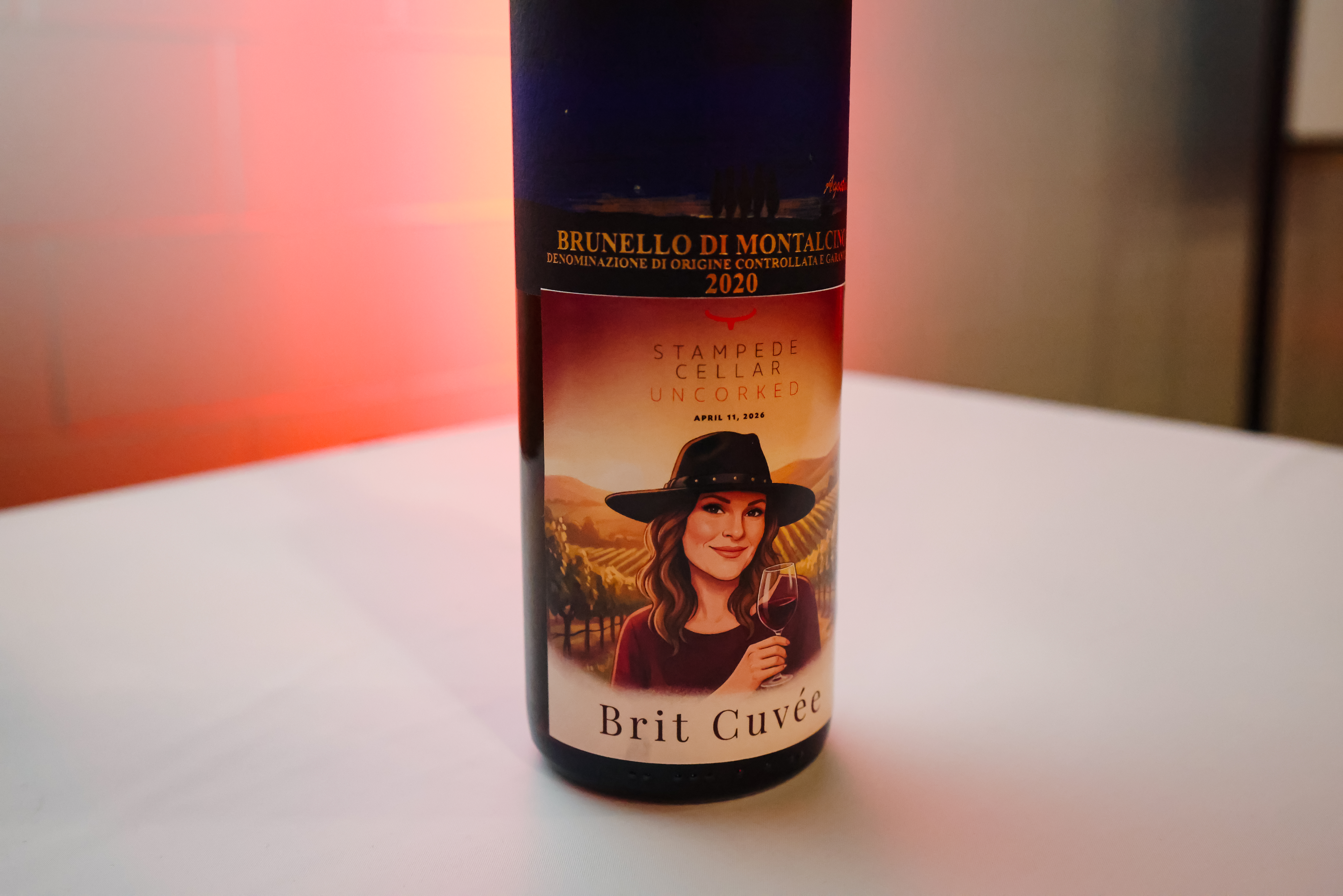 Custom wine label featuring a woman with a hat, labeled "Brit Cuvée," showcasing the event branding for Stampede Cellar Uncorked 2023, with a scenic vineyard background.