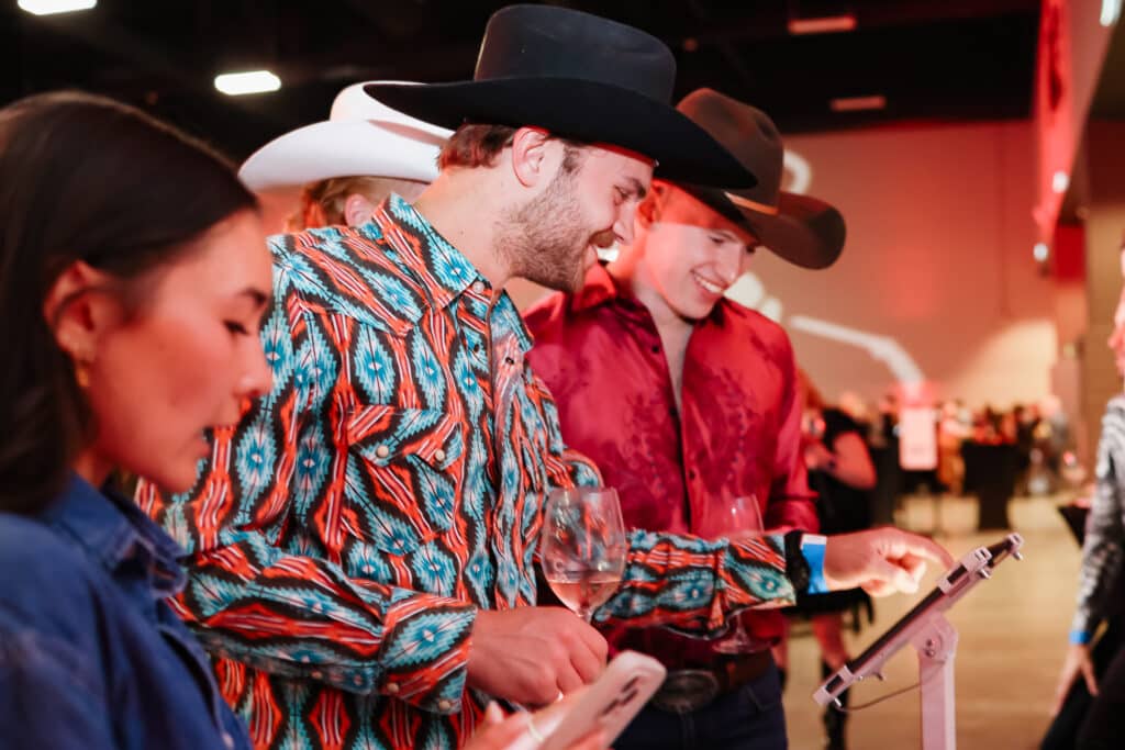 Two men wearing cowboy hats looking at photos on a tablet at an event