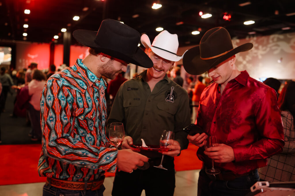 Three men wearing cowboy hats and holding wine glasses at an event