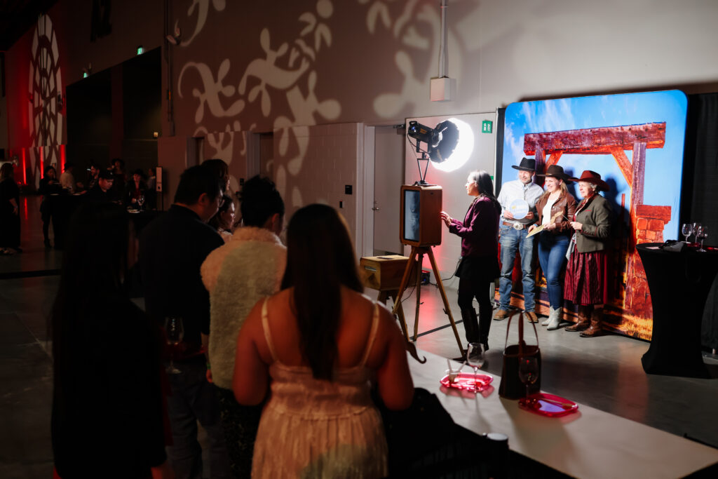 Guests engaging at a print-on-site photo booth with a western-themed backdrop, capturing memorable moments at the Calgary Stampede event, featuring a photographer and participants in cowboy hats.