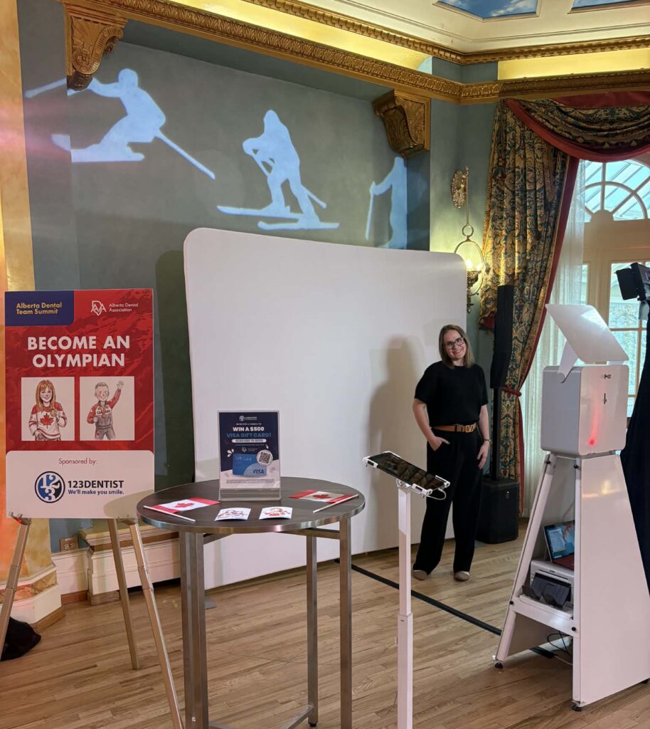 AI photo booth setup at Alberta Dental Team Summit featuring a smiling woman, interactive display, promotional materials, and skiing projections on the wall.