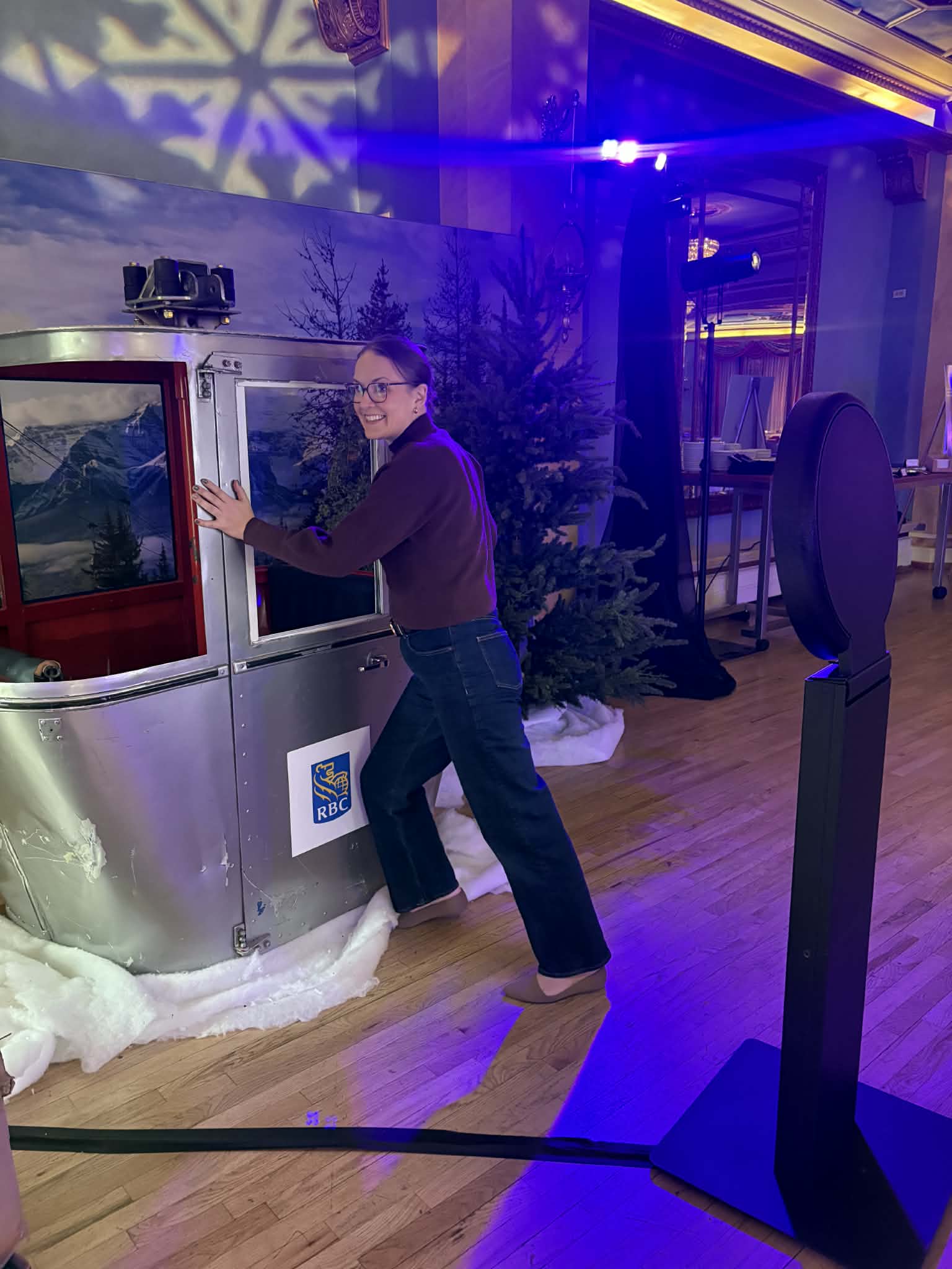 Woman interacting with a photo booth featuring RBC branding, set against a backdrop of snowy mountains and trees, illuminated by colorful lighting, at an event promoting engagement and brand visibility.