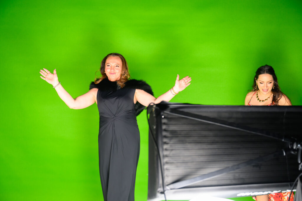Two women posing in front of a green screen during a cinematic runway experience at the Red, White & Gold Gala, showcasing the event's interactive video setup.