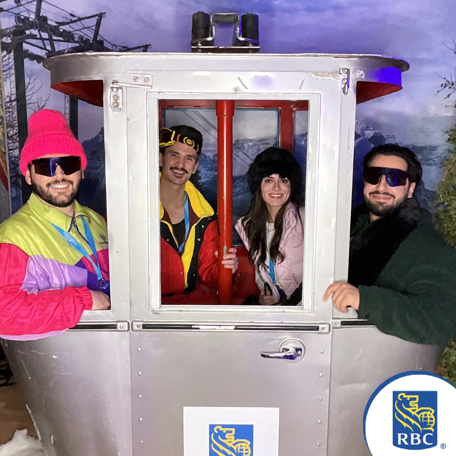 Group of four people in colorful winter attire posing inside a photo booth designed as a ski gondola, featuring RBC branding.