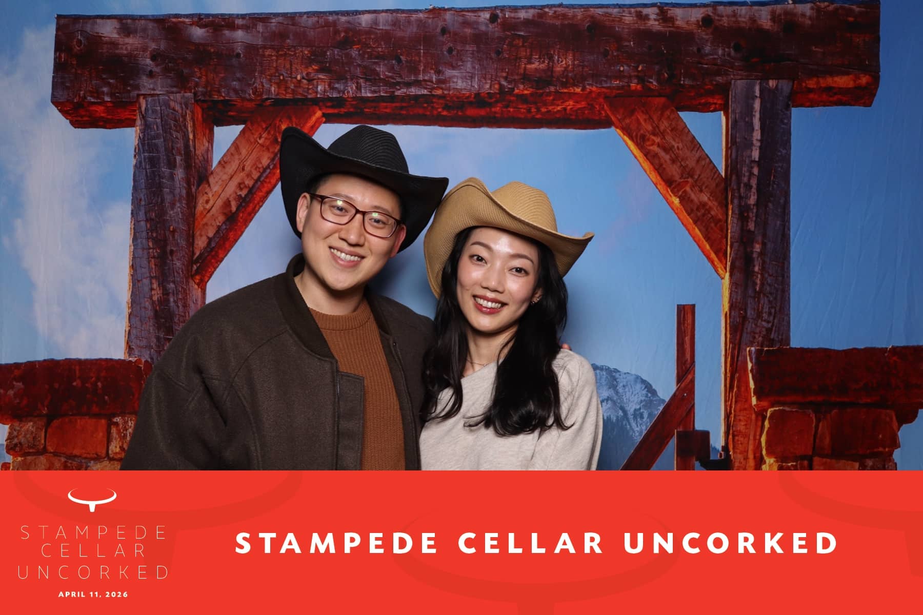 Couple wearing cowboy hats posing in front of a rustic backdrop at the Stampede Cellar Uncorked event, featuring event branding and a vibrant atmosphere.