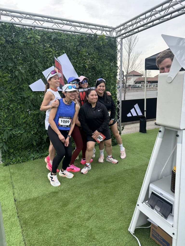 Experiential marketing photo booth at Calgary event with Adidas branded backdrop and runners posing for photos.