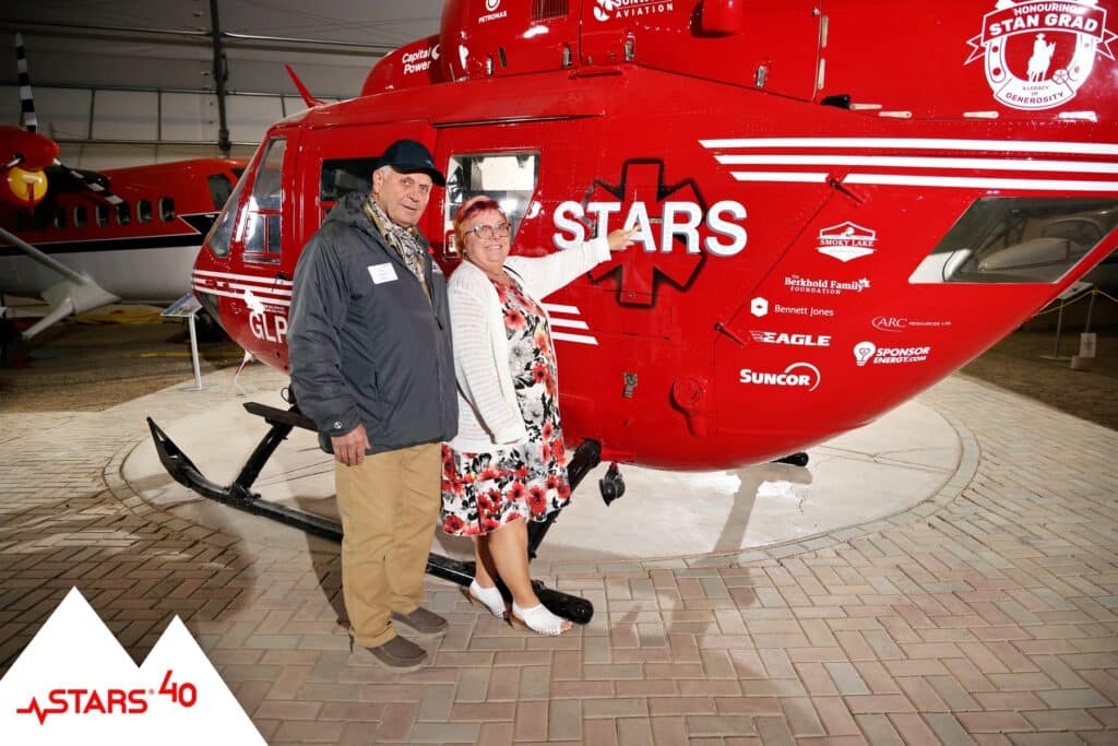 Guests posing for portraits with the STARS helicopter, donor recognition branding and logos visible.
