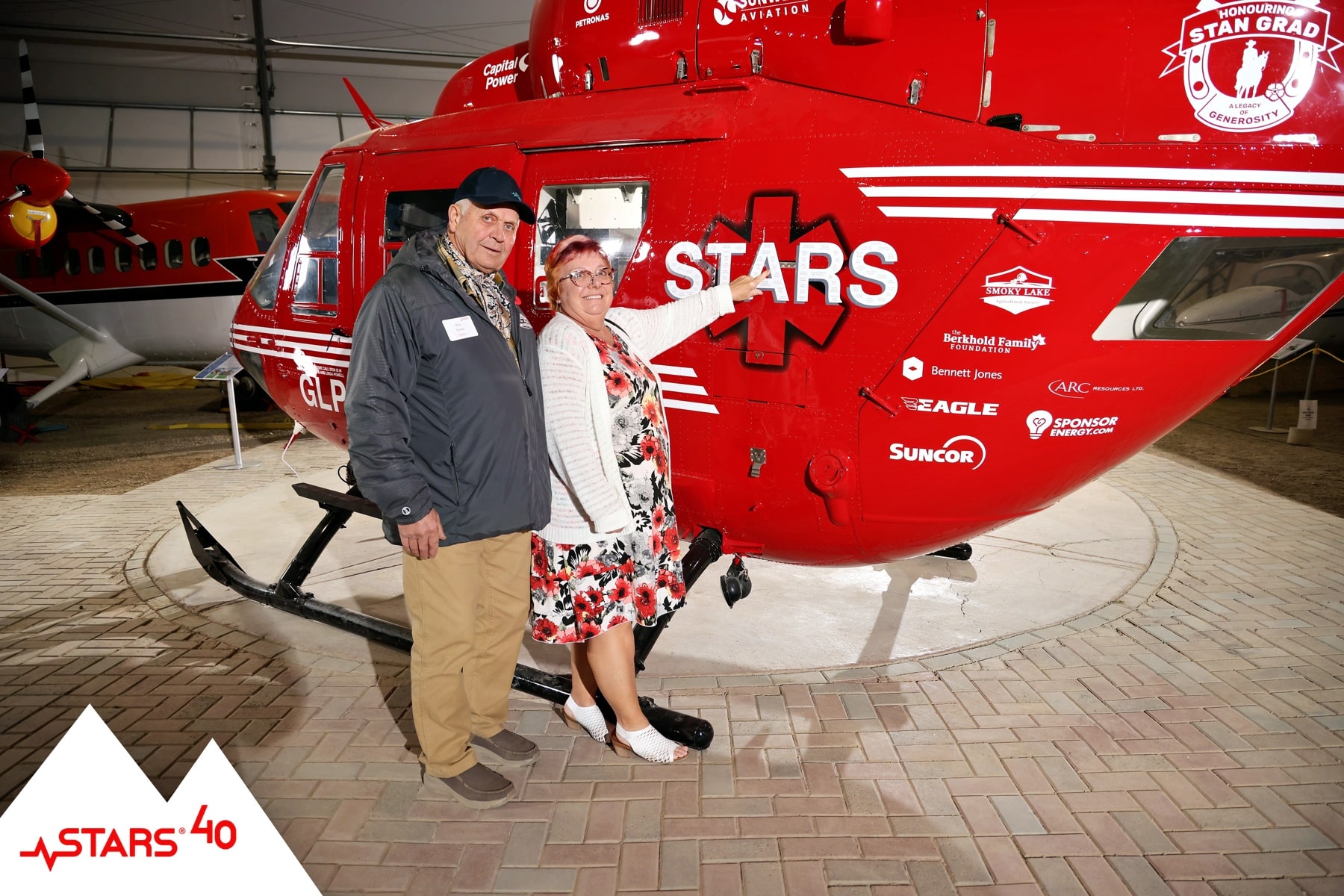 Guests posing for portraits with the STARS helicopter, donor recognition branding and logos visible.