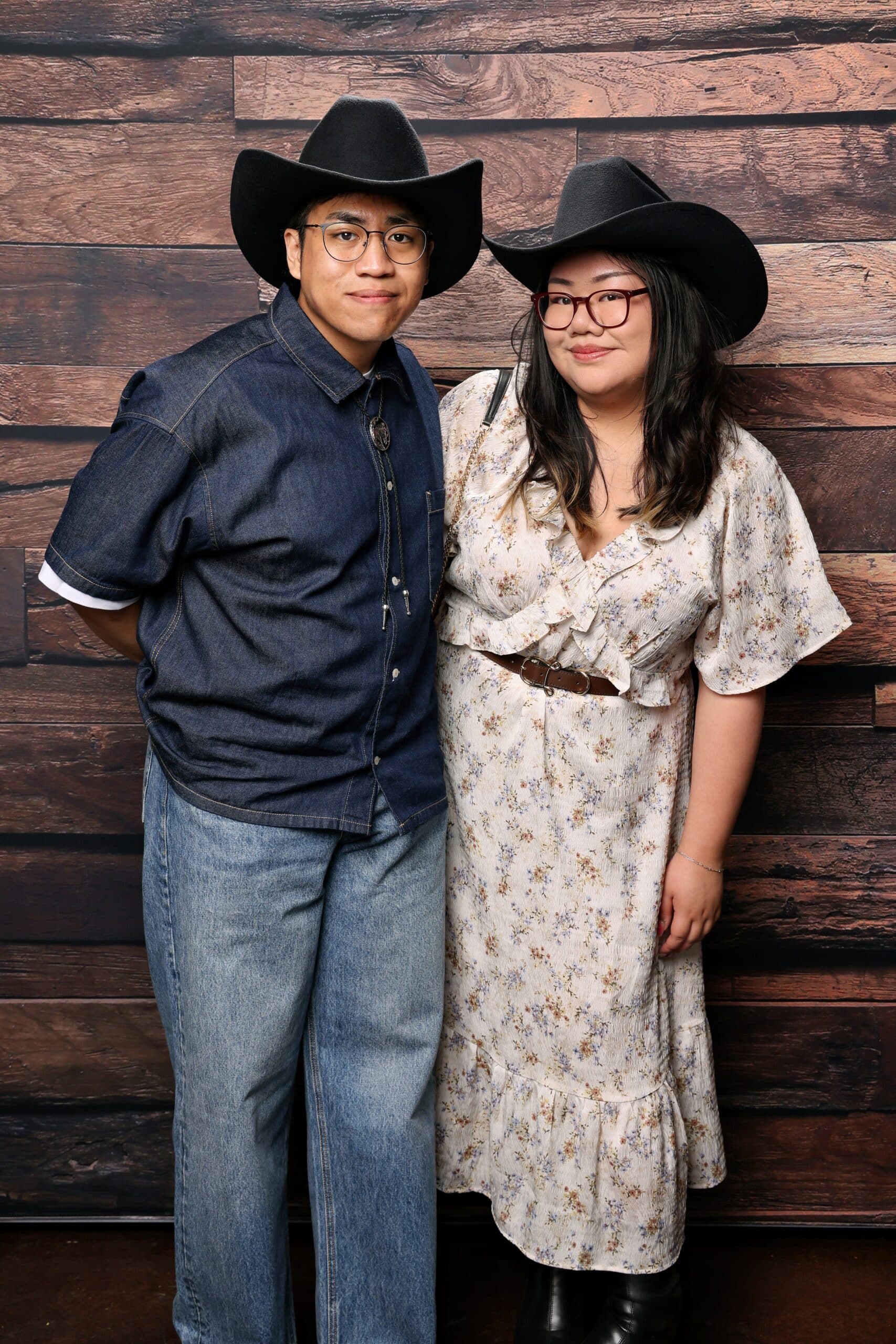 Couple wearing cowboy hats posing together in front of a rustic wooden backdrop, capturing the